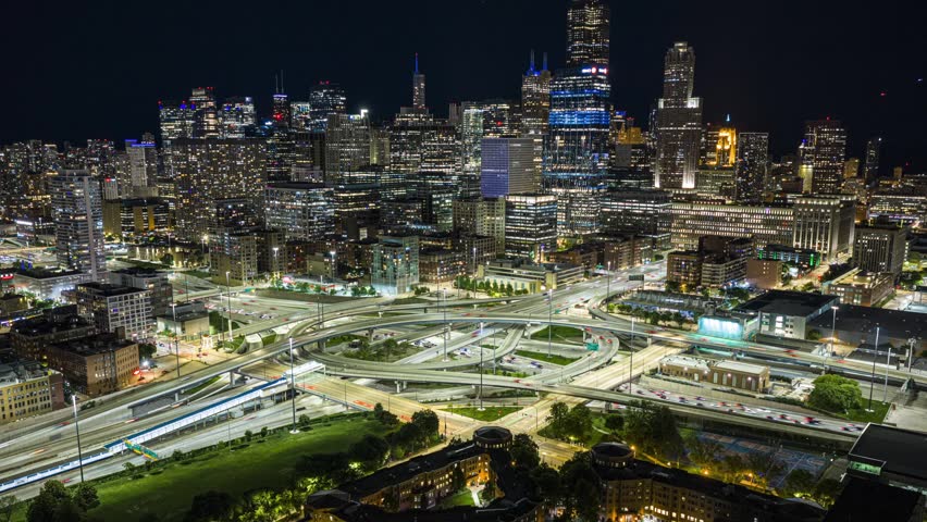 Night aerial time lapse showing downtown Chicago skyline with skyscraper and illuminated highway intersection creating light trails, urban development and transportation