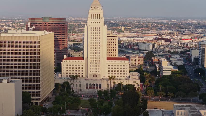 Los Angeles City Hall standing tall in urban downtown landscape with sprawling city extending towards hazy horizon and buildings catching warm morning sunlight