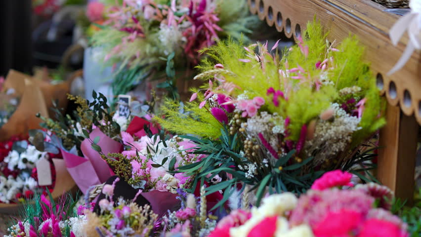 Woman browsing a vibrant selection of beautifully arranged dried flower bouquets at a local florist shop or outdoor market stand
