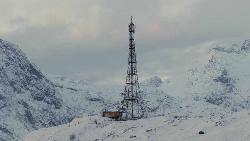 Metal radio tower and wooden utility hut on snowy alpine ridge
