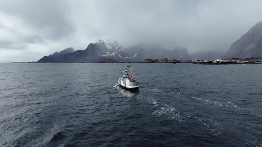 Fishing boat sailing toward rocky misty shoreline under overcast skies