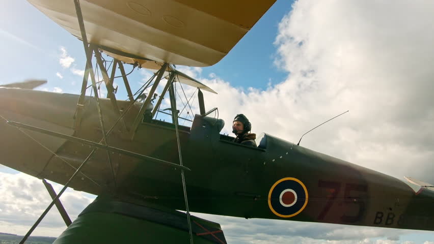 World war two military biplane flying in a cloudy blue sky with the sun flaring