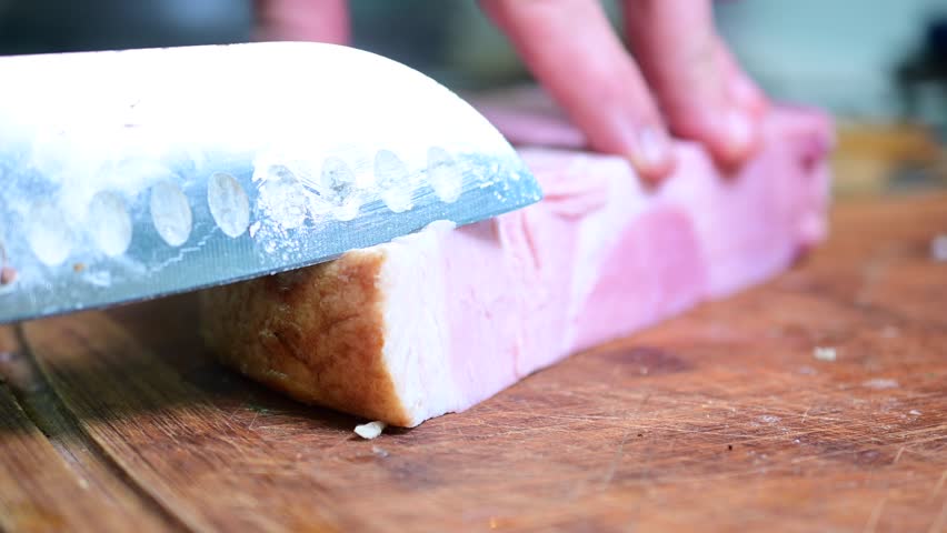 up close cutting ham, cutting board man close up of a knife slicing good chunk of ham cold cut meat