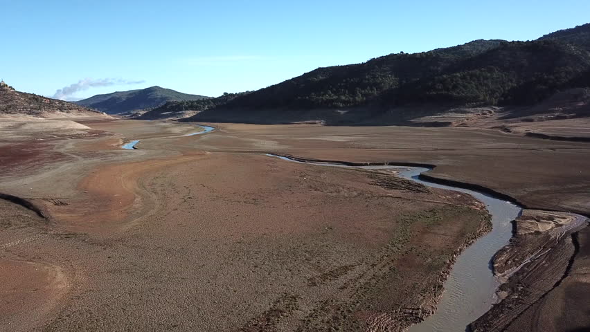 Aerial footage of Entrepeñas reservoir near Sacedón in Guadalajara Spain at extreme low water levels due to severe drought. The dried lake bed exposes red soil, petrified trees and submerge structures