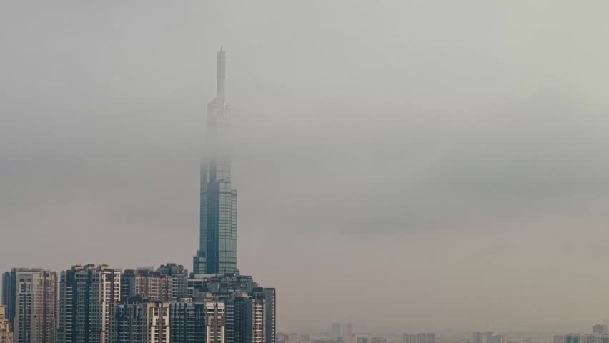 Tracking shot skyscraper rising through low fog above dense residential high rise skyline in urban district, Ho chi minh city in Vietnam.