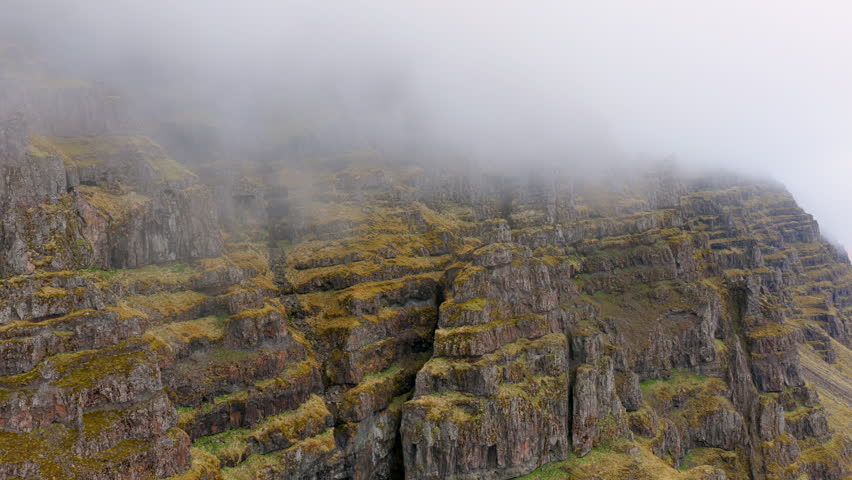Misty cliffs landscape. Dense fog blankets rugged Icelandic cliffs and lush mossy plateaus in scenery