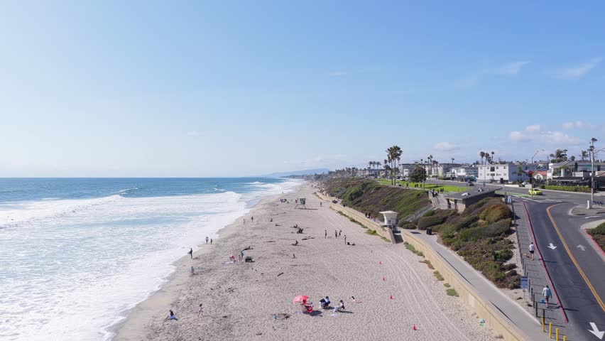 Carlsbad State Beach featuring vibrant green bluffs and people walking along ocean coastline and sandy shoreline with gentle breaking waves on sunny day in California