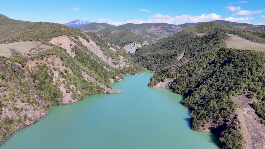 Aerial camera shifts leftward over the deep turquoise water of Shkopet Lake reservoir, framing the steep mountain slopes and pristine natural wilderness of the Mat Gorge