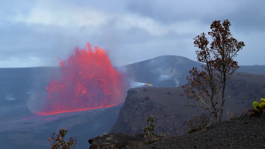 View of Halemaumau Crater with a glowing lava fountain erupting against a cloudy sky in Hawaii County, Hawaii, United States.