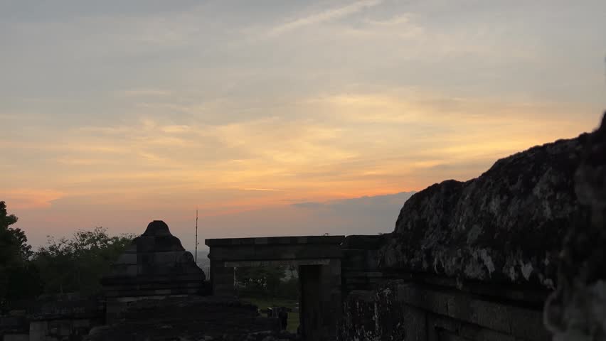 Beautiful orange sunset sky over ancient stone ruins of a historical temple site at dusk.