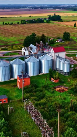 Aerial grain silos and farm buildings surrounded by open countryside, drone vertical orbit overview