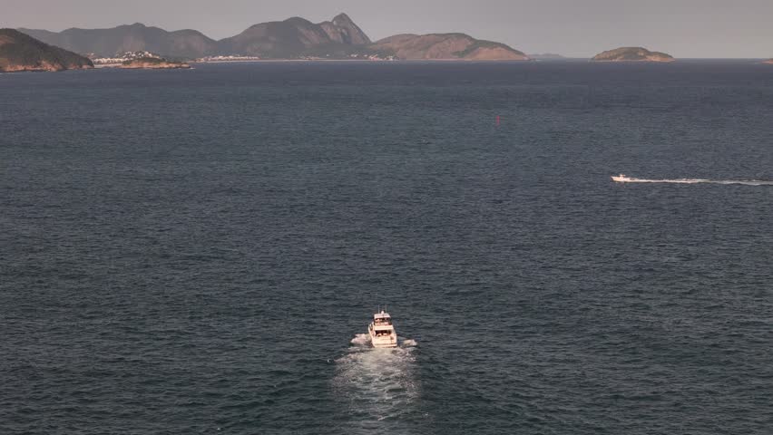 View of Guanabara Bay with a white boat cruising through the blue waters and lush green mountains in the background in Brazil.