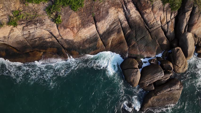 View of waves crashing against the rocky coastline and large boulders of Guanabara Bay, Brazil.