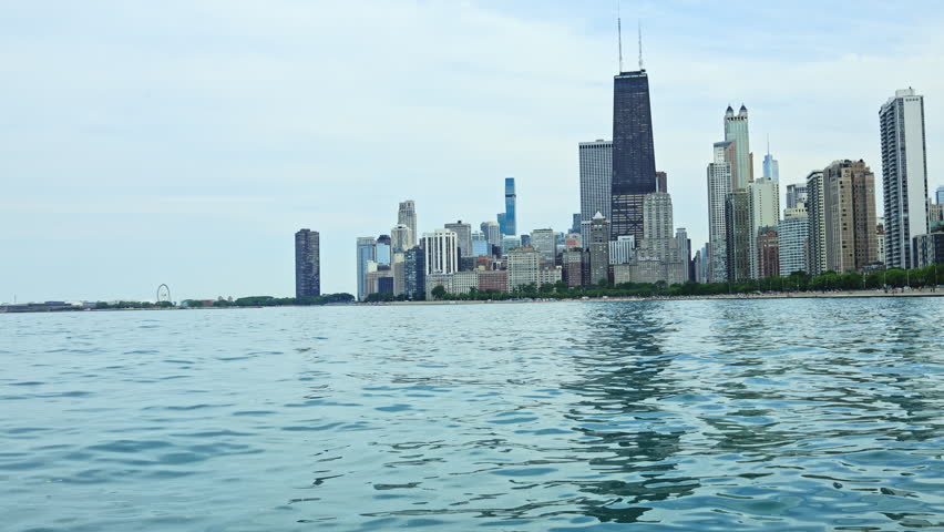 Chicago skyline rises above Lake Michigan on a bright day. The water reflects the tall buildings and the city atmosphere. People enjoy time by the lakefront.
