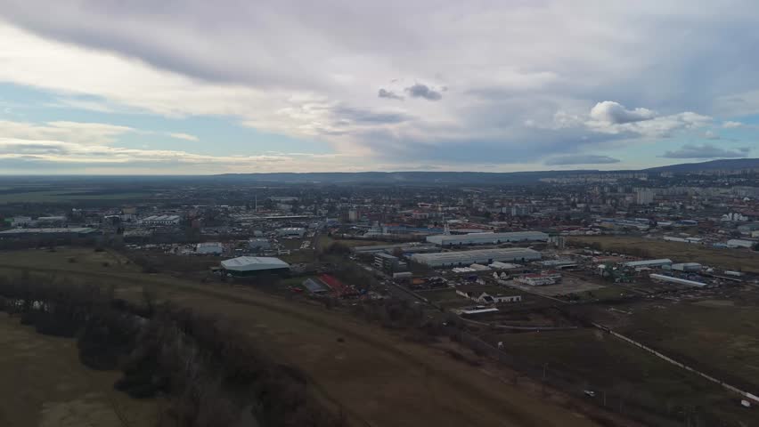 In Miskolc, a drone captures a wide view of residential apartments, industrial facilities, and surrounding hills under cloudy skies along the city