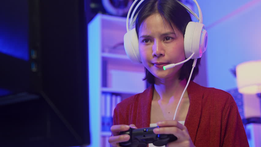 Excited young Asian girl playing video game with headset and joy stick controller at home.