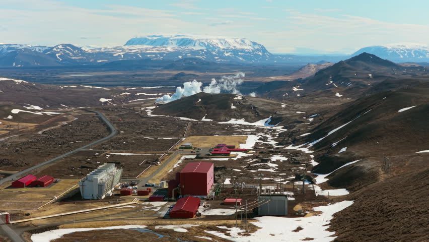 Steam emanates from volcanic site. Vast geothermal installation amid volcanic and mountain scenery