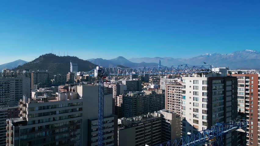 Ascending shot over dense urban residential district revealing city skyline with Costanera Center tower, San Cristobal Hill and snow-capped Andes. Santiago, Chile