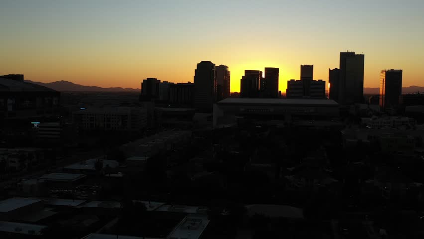 Aerial view of the Phoenix city skyline silhouetted against a vibrant sunset sky with distant mountains and urban buildings Phoenix, Arizona, United States.