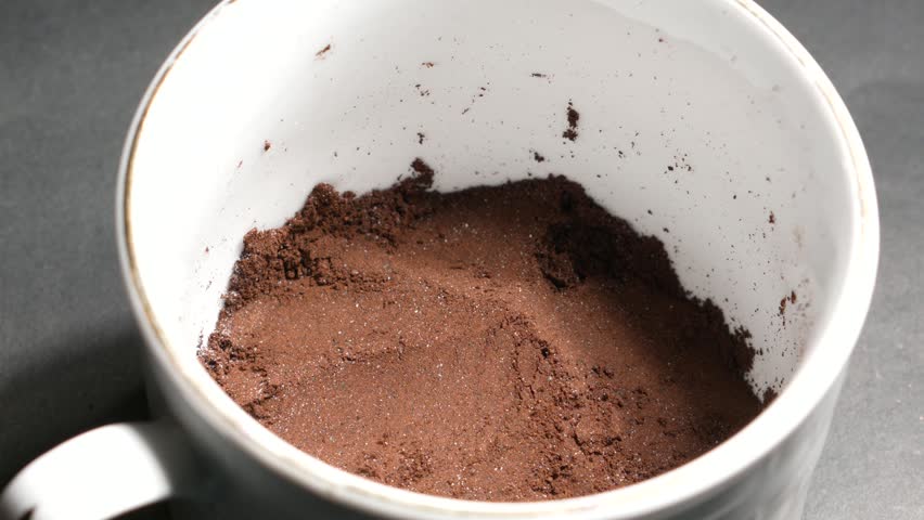 Pouring hot water into a white mug with ground coffee, brewing a drink.