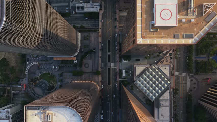 Top down push in aerial of downtown Los Angeles skyscrapers with city street traffic moving below and golden hour sunlight creating deep shadows on building facades