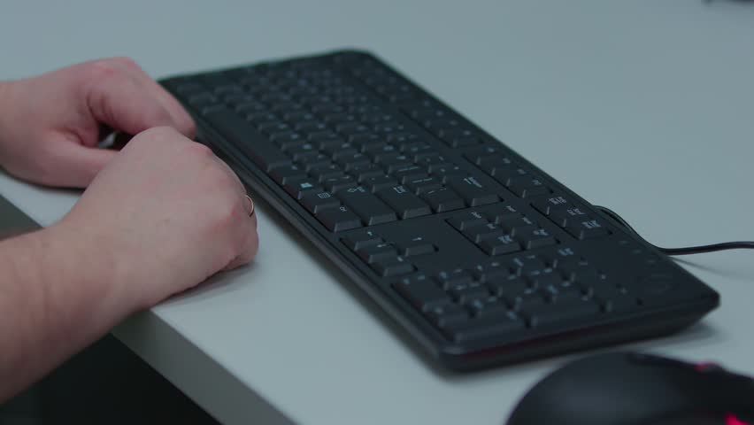 A person is typing on a keyboard. The keyboard is black and has a red key on the top left