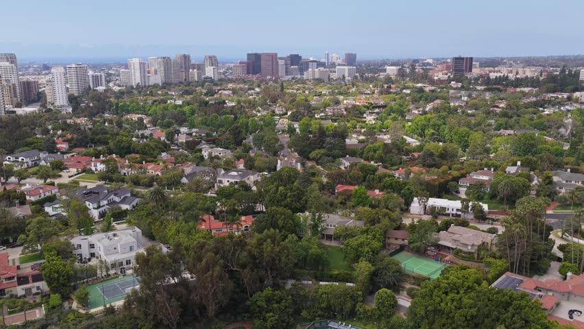Affluent Beverly Hills neighborhood with luxury homes and mansions revealing Century City skyline in Los Angeles, California during day