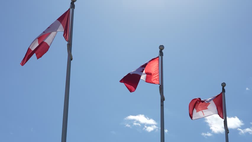 Three red and white flags waving on tall poles against a bright blue sky