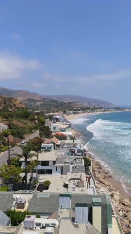 Malibu California coastline showing luxury beachfront real estate properties and Pacific Ocean on sunny day with blue sky, representing wealthy lifestyle