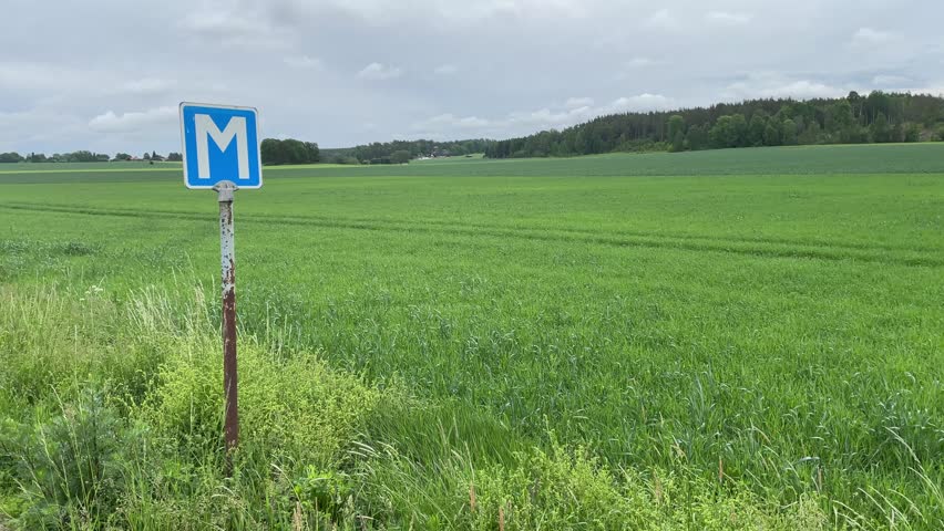Swedish meeting place sign for cars at small country side road. Next to a green landscape with large grass field. Bålsta, Sweden.