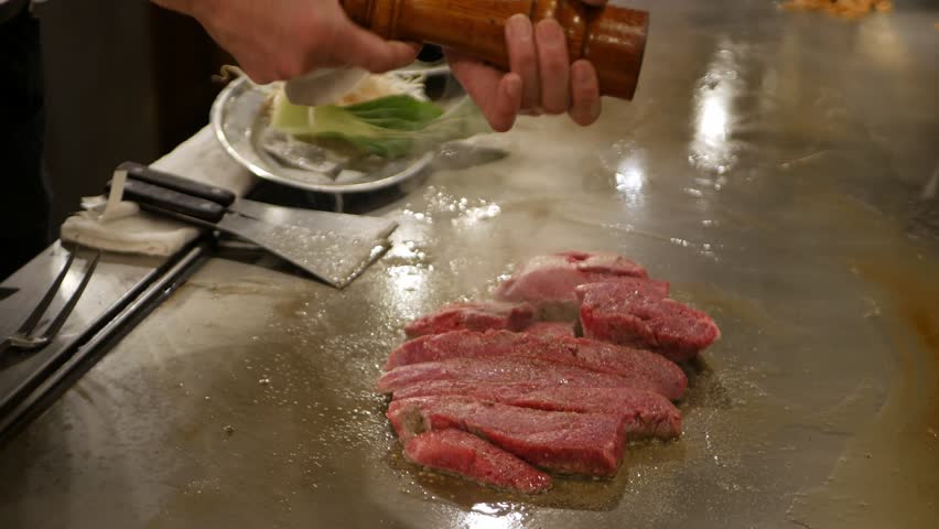 POV to kobe sirloin wagyu steak while cooking on teppan yaki flat pan in japanese style restaurant for lunch time. Chef cooking wagyu kobe beef sirloin steak on teppanyaki flat pan