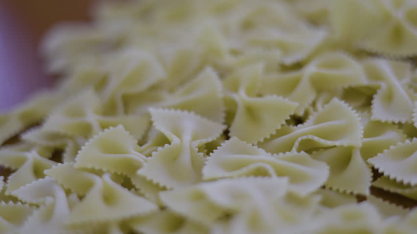 Uncooked Bow Tie Pasta On Table Dry. Close up of farfalle macaroni dropping into a ceramic bowl, suitable for italian food commercials or cooking tutorial videos.