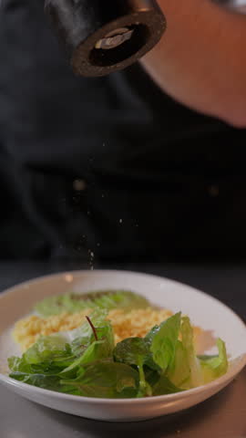 Close-up of a chef adding freshly ground black pepper to a healthy balanced meal with fresh greens and protein-rich ingredients. Modern nutritious dish preparation and restaurant food presentation