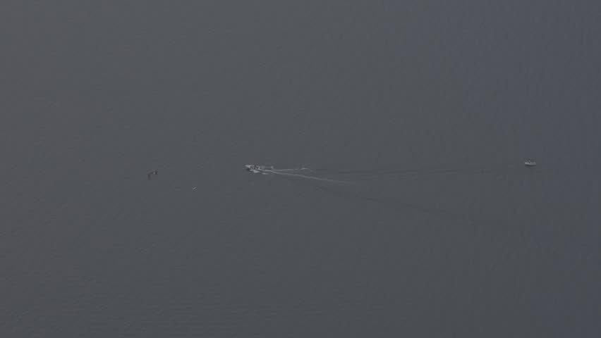 Aerial view of a small motorboat moving across calm blue lake water, leaving a subtle wake behind. Minimalist travel and transportation scene with vast open water, copy space and peaceful atmosphere.