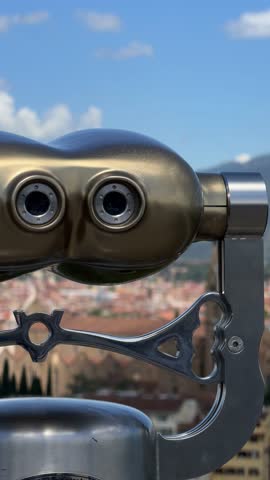 Scenic view of Florence, Italy, captured through a telescope overlooking the city skyline with historic buildings and mountains in the background under a clear blue sky