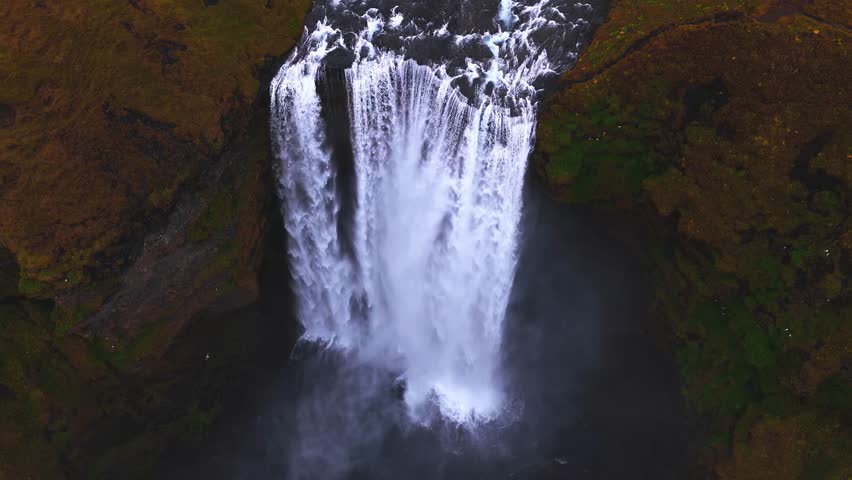 Powerful waterfall creating dynamic motion as water drops from a rugged cliff into a deep pool below. Birds soar over the impressive natural landscape, highlighting the scale and wild beauty.