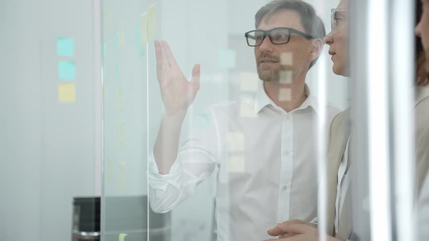 Business colleagues collaborating on a glass board in an office, discussing strategy, sharing ideas, and brainstorming during a productive meeting for project development