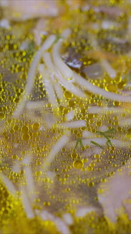 Appetizing mushroom noodle dish with herbal garnishes and shimmering oil droplets. Closeup of steaming mushroom noodles in rich golden broth with herbs and glistening oil droplets