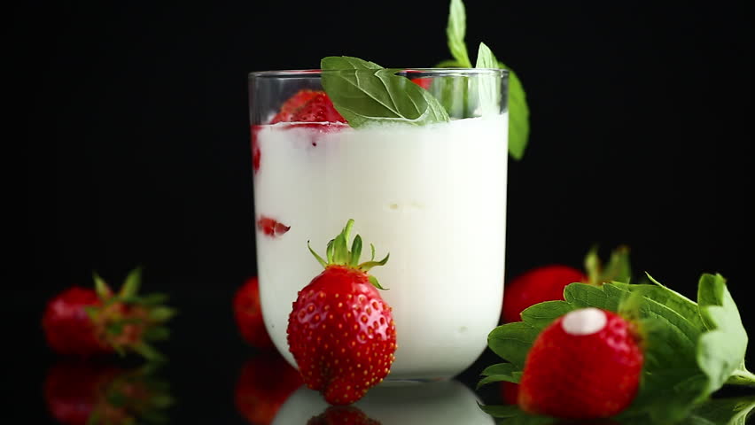 Fresh strawberry yogurt dessert with floating berries on black background.