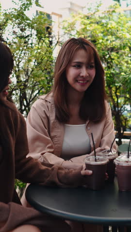 Two young asian women laughing and talking at an outdoor cafe