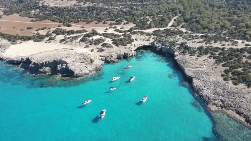 Boats are sailing into a turquoise cove surrounded by rocky cliffs. The footage shows a scenic aerial view of the