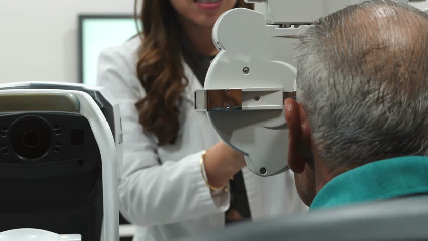 Female medical professional in a white coat conducting a health check-up on an elderly male patient using specialized diagnostic machinery in a modern, well-equipped examination room