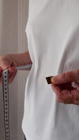 Senior woman measuring waist with tape measure, weight loss and healthy lifestyle concept.