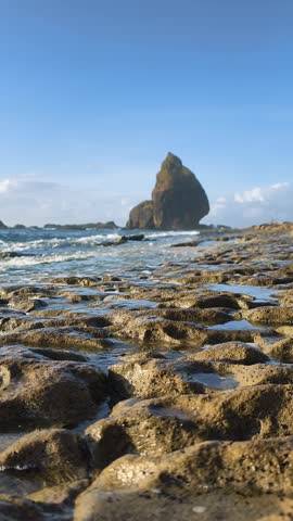Scenic coastal landscape with mossy reef rocks in the foreground and powerful sea waves washing the shore near giant rock formations. Sunny day beach.