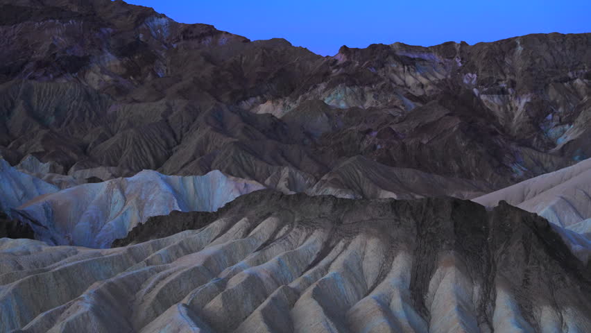 Rugged eroded badlands formations Zabriskie Point in Death Valley intricate ridge patterns during twilight. Layered sedimentary rock creates dramatic textures across the barren desert landscape.