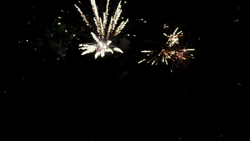 Red and gold fireworks explode overhead against a black sky, with glowing trails, drifting smoke, and sparkling bursts creating a festive celebration atmosphere