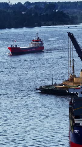 Cargo ships and tugboat operate on a wide river near an industrial port facility