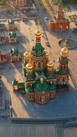 Vertical video. Yoshkar-Ola, Russia. The Cathedral of the Annunciation of the Blessed Virgin Mary stands as a striking Russian Orthodox landmark on Republic Square, its five gilded onion domes and richly decorated brick facades catching the warm light of late afternoon. Built between 2009 and 2014 and consecrated in 2016, the cathedral fuses architectural elements reminiscent of both Saint Basil