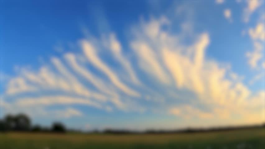 Blurry image of wispy clouds in a blue sky over a field