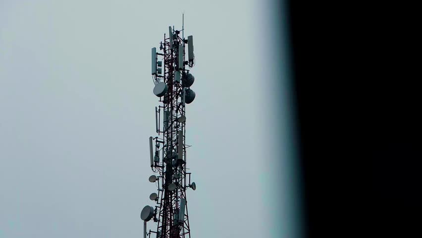 High telecommunication tower stands tall against a muted sky. Metal lattice holds many satellite dishes and antennas.